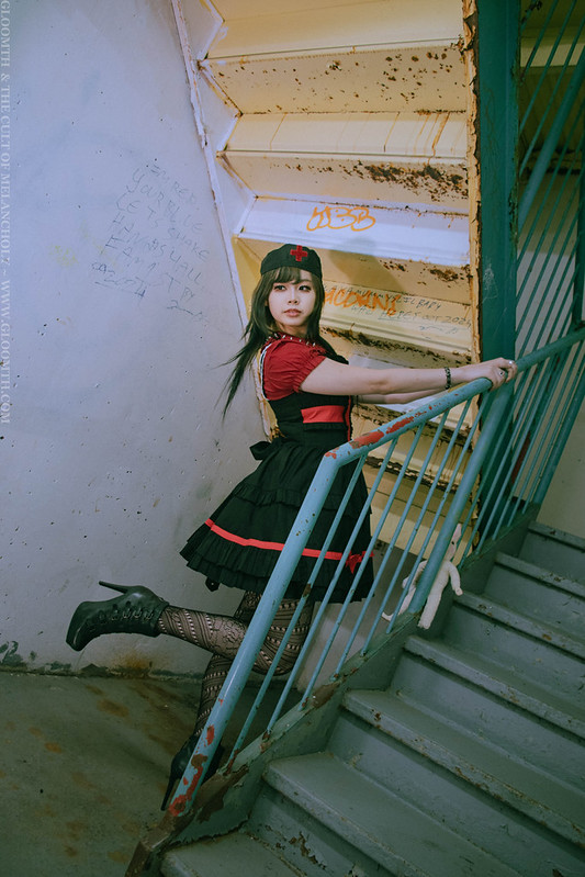 gothic model in a red and black dress posing in an abandoned stairwell