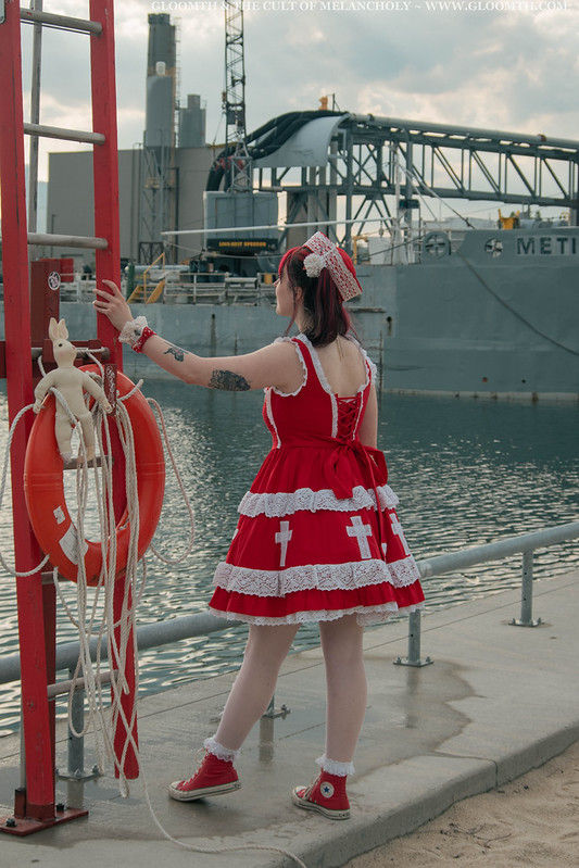 lolita in a red jsk posing with a large industrial ship